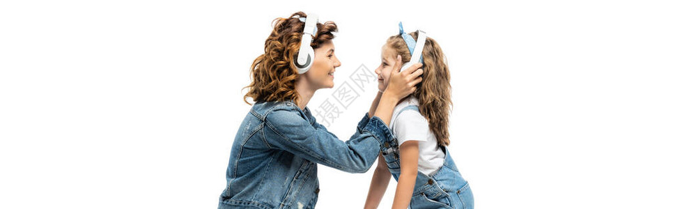 母亲和女儿的侧面戴尼姆服装用耳机对面听音乐在白色全景镜图片