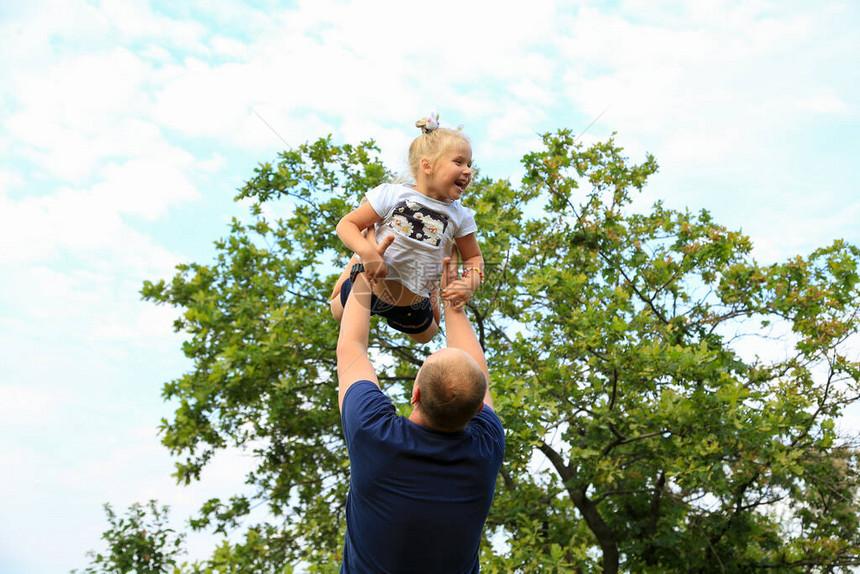 一位父亲把他三岁的女儿扔到头上女儿高兴地笑了飞行愉快乐的女儿和父亲一个幸福的家庭野营温暖的图片