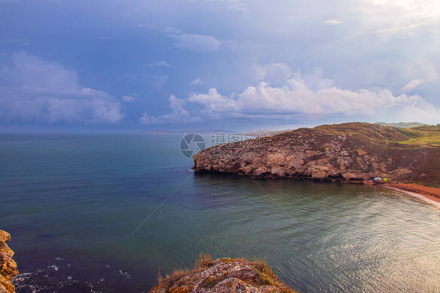 岩石海岸的美丽景色陡峭悬崖的海岸晒黑的绿草间的小径乌云密布的蓝天秋日早图片