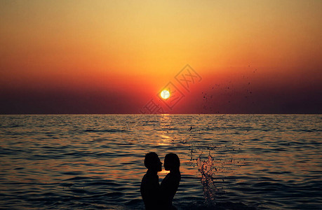在海滩拥抱的年轻夫妇的日落剪影图片