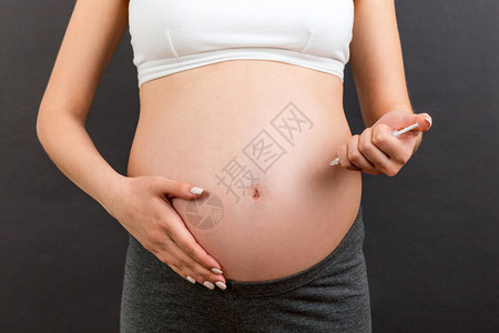 关闭孕妇在她的腹部注射胰岛素在五颜六色的背景与复制空间怀孕期间图片