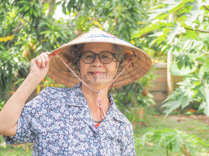 一位戴着帽子的亚洲高级女站在花园里微笑着看相机的肖像文本的空间老人和医图片