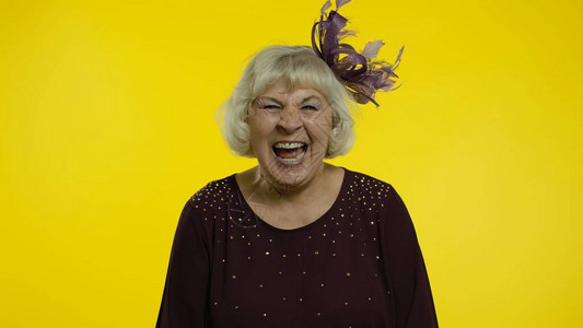 快乐的老妇人在听到荒谬的轶事有趣的笑话感到无忧虑有趣积极的生活方式后大声笑了起来黄色背景中的图片