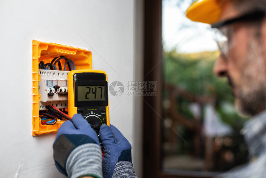 与测试仪一起工作的电工测量住宅安装的电气面板中的图片
