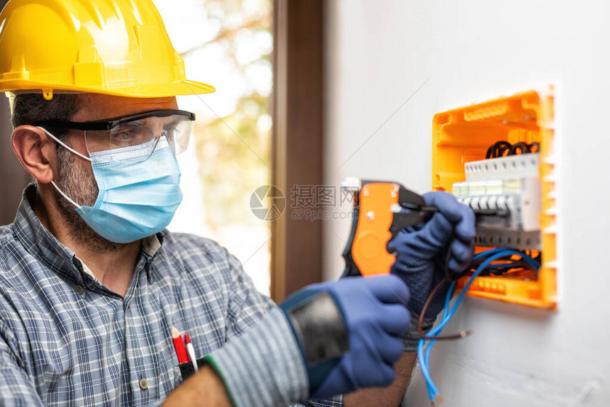 电工在受头盔护目镜和手套保护的电气面板上工作图片