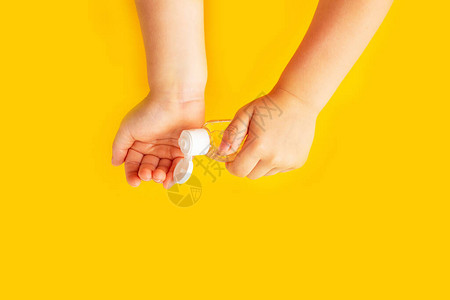 儿童的手拿着一瓶黄色背景的透明洗手液凝胶孩子们的卫生手卫生细菌和病图片