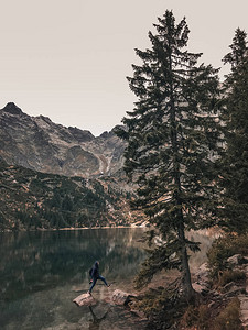 站在一块被高山和树木环绕的清澈湛蓝绿色湖泊中间的大石头上图片