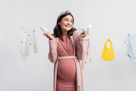 快乐的孕妇拿着小靴子靠近婴儿衣服衣服线图片