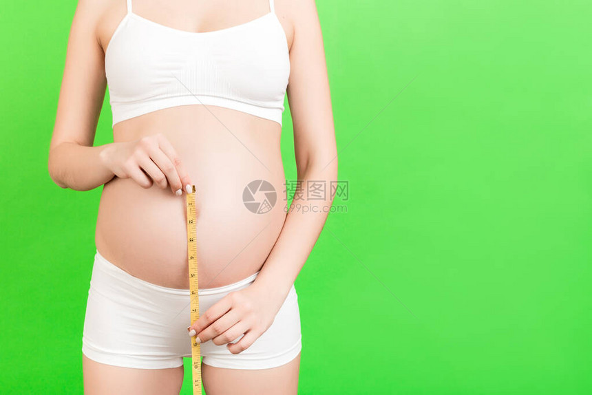 白内衣孕妇在绿色背景下生长的腹部测量其生殖器的切片图像图片