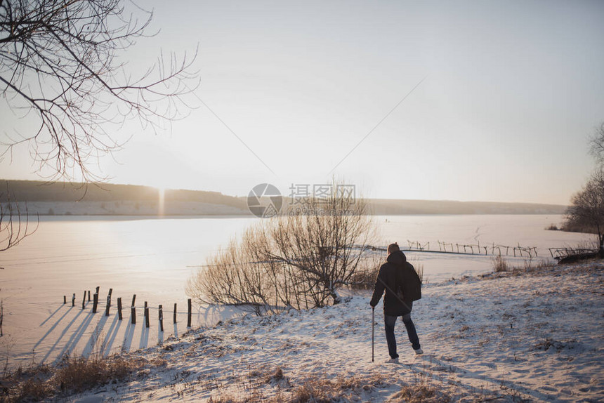 一个拿着棍子的人站在冰雪下看着一条结冰的河流严寒冬所有的土地都被白雪覆盖艳阳高照有图片