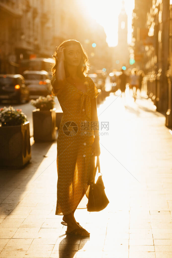 一位身穿黄色连衣裙领口低垂的可爱年轻女子手拿皮包图片