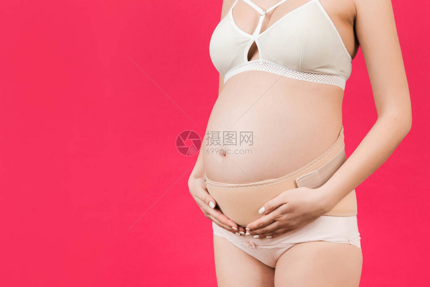 近身穿内裤的孕妇在粉色背景和复制空间使用孕带图片