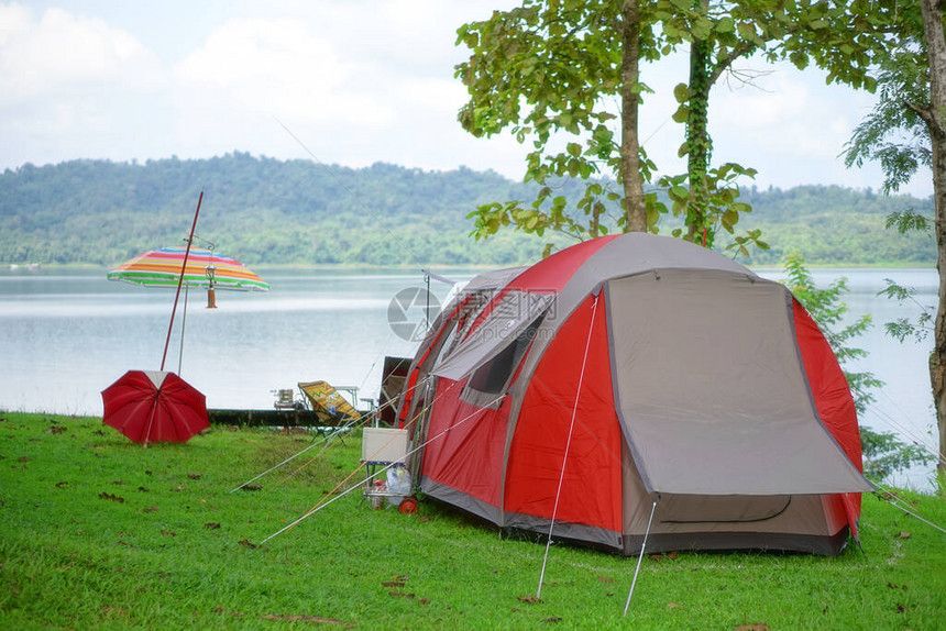 自然景观红色野营帐篷和五颜六色的雨伞在绿草地或公园的树下有湖泊或河流和树山丛林图片