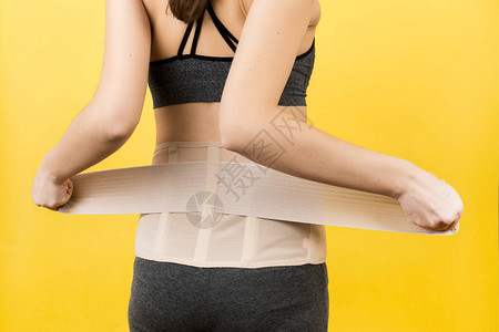 孕妇穿着矫形紧身胸衣使背痛在黄色背景下消失的后视图图片