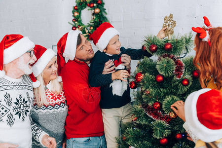 父亲与家人一起装饰圣诞树时将儿子握图片