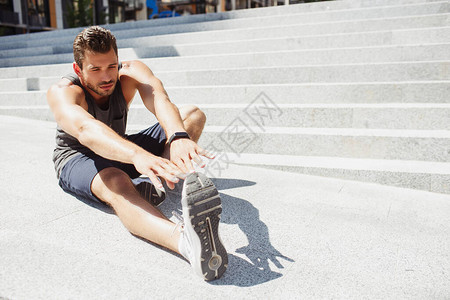体育运动员坐在台阶旁伸展手臂和腿部的景象图片