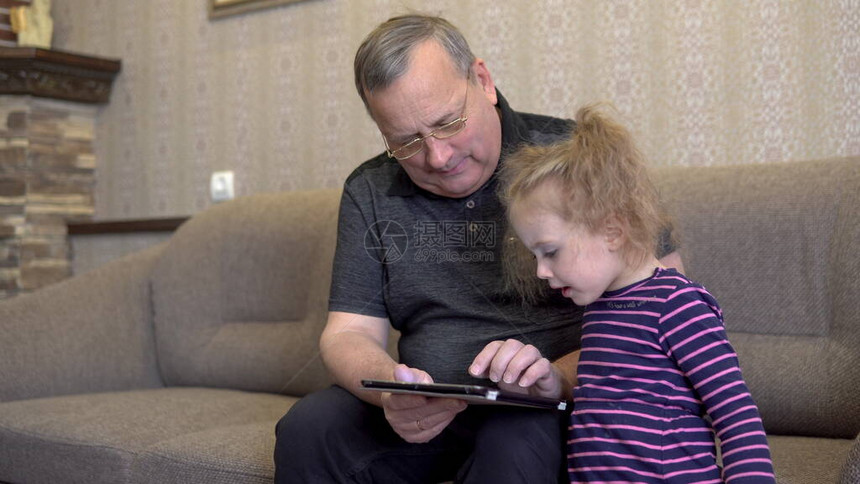 孙女和祖父正坐在平板电脑旁女孩皱着眉头看着平板电脑一起坐在沙图片
