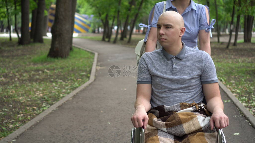 一名妇女驾驶一名在轮椅上患有肿瘤病的青年男子驾车穿过公园图片