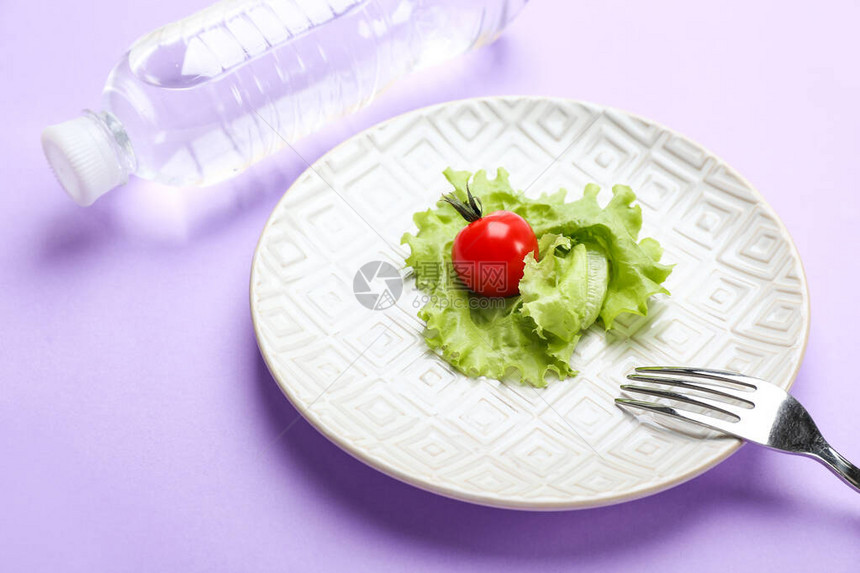 有蔬菜叉子和瓶装水的盘子在颜色背景图片