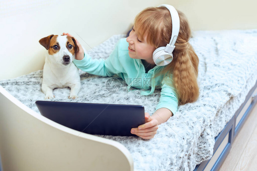 与狗一起躺在床上听音乐或视频课的可爱小女孩线上教育电子学习概图片