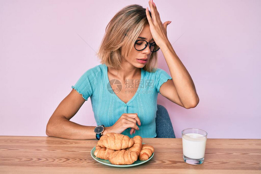 早餐吃羊角面包的美丽白种女人因错误而惊讶地用手捂着头图片