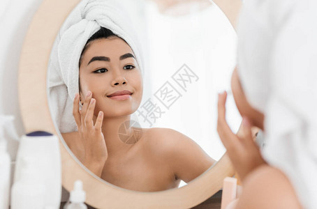 快乐的亚洲年轻女子在她脸上涂抹美容产品图片