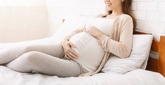 平静的孕妇抚摸肚子睡在家中全景图片