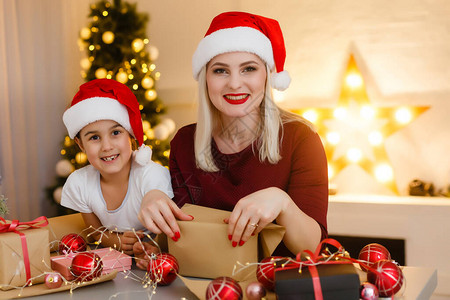 快乐漂亮的母亲和她可爱的小女儿坐在办公桌前享受手工制作的圣诞装饰之美图片