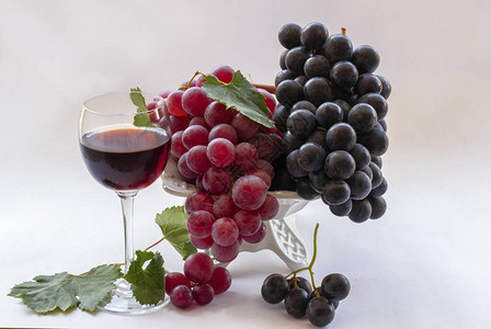 白色背景上的红黑葡萄和玻璃杯中的红酒图片