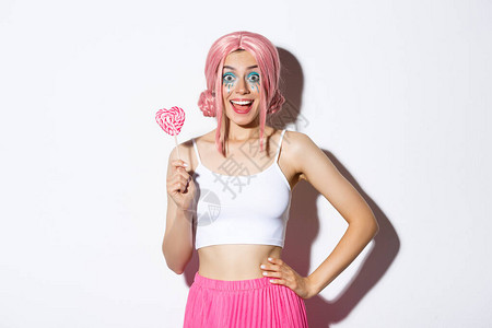 穿着粉红色假发的美丽笑脸女孩拿着心形糖果戏法或用童话服在圣殿里治疗站图片