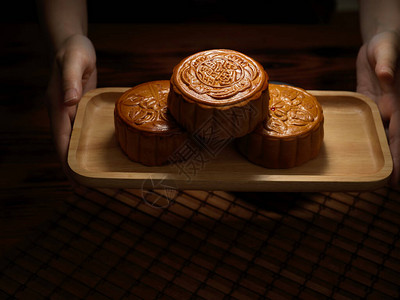 近距离观看手握着传统月饼的木盘月饼上的中文代表英语中的五内核和烤图片