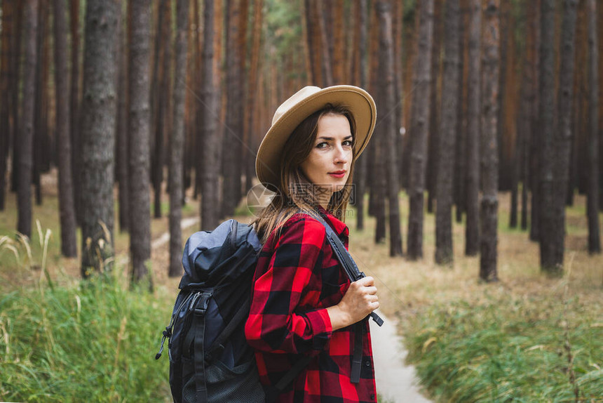 穿着帽子红衬衫和背包的年轻女人在森林图片