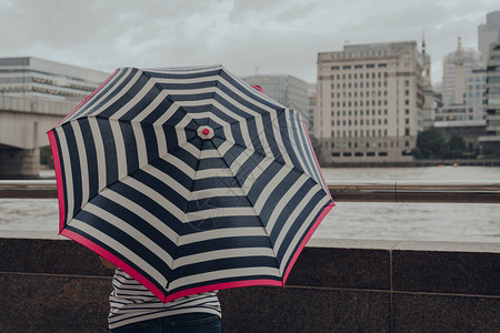看着英国伦敦泰晤士河旁的带条纹雨伞的不明身份妇女图片