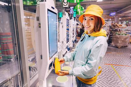 快乐的年轻女顾客在现代超市自助动售货机结帐时购买和支付一瓶橙汁图片