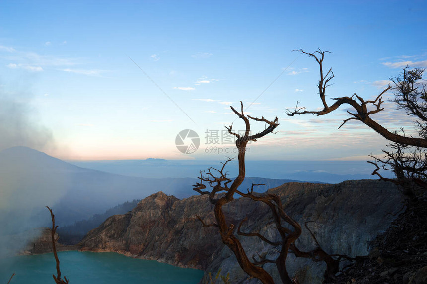 印度尼西亚KawahIjien火山美丽的日出硫磺湖山顶上的枯树柔和的焦点冒险旅行概念山图片