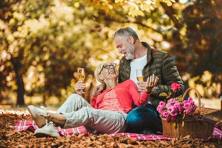 快乐的老年夫妇在秋季公园野餐敬酒图片