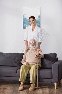 快乐的社会工作者触摸着坐在沙发上用拐杖坐着的高图片