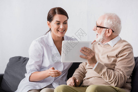 快乐的老人向兴奋的社会工作者展示数字平板电脑图片