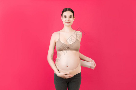 孕妇穿矫形绷带以减轻背部疼痛的粉红色背景和复制空间的肖像骨科腹图片