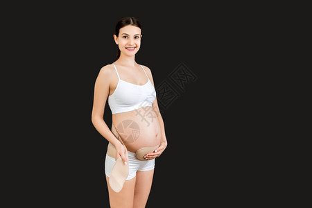 穿着白色内衣的孕妇在黑色背景下穿着孕妇腰带图片