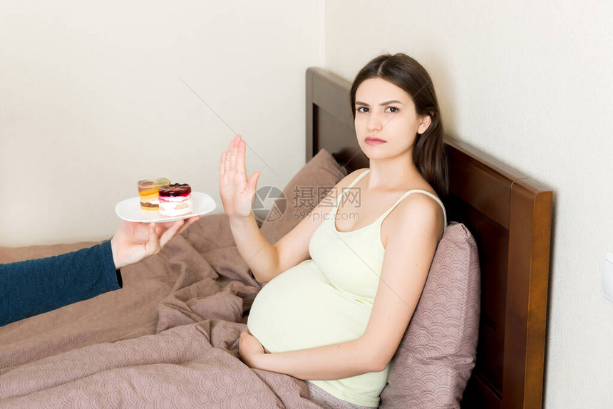 躺在床上的孕妇不想吃蛋糕并做出停止的手势怀孕期间没图片