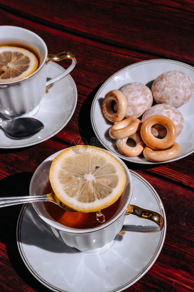 一个美丽的白碗里放着柠檬和糖果的红茶站在一张木桌上用小茶匙搅拌茶中图片