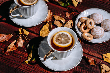 配有茶和柠檬小白碟上的茶点心和糖果秋天的落叶和茶会在一张木桌图片