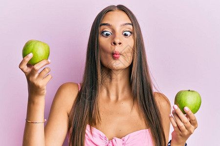 年轻的西班牙女人拿着绿苹果用嘴和斜眼做鱼脸疯狂图片