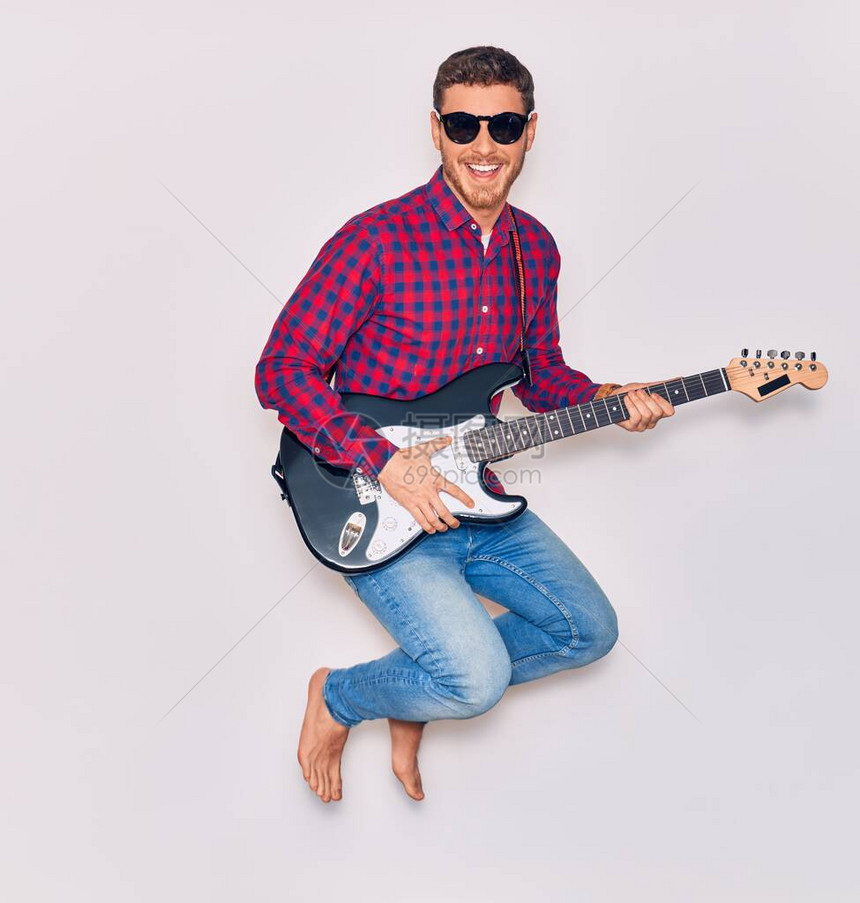 穿着太阳镜的英俊年轻英俊的西班牙裔艺术家男子笑着快乐地弹电吉他图片