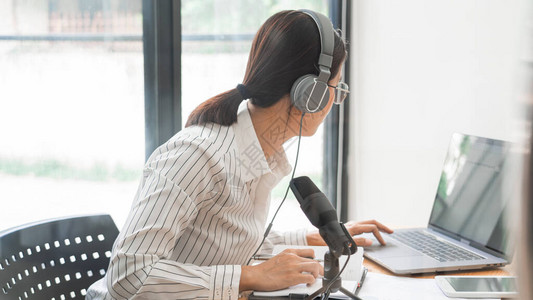 亚洲女播客并在工作室使用耳机专业麦克风和桌上的电脑笔记本电脑录制在线脱口秀节目背景图片