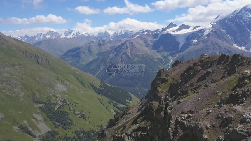 山顶上旅行者的空中景象与绿草覆盖的斜坡飞过山顶和令人惊叹的山峰图片