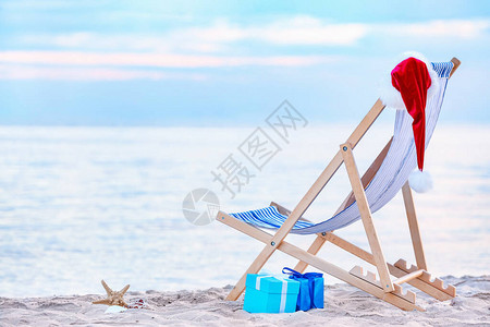 海边的沙滩椅礼物和圣诞帽圣诞假期概念图片