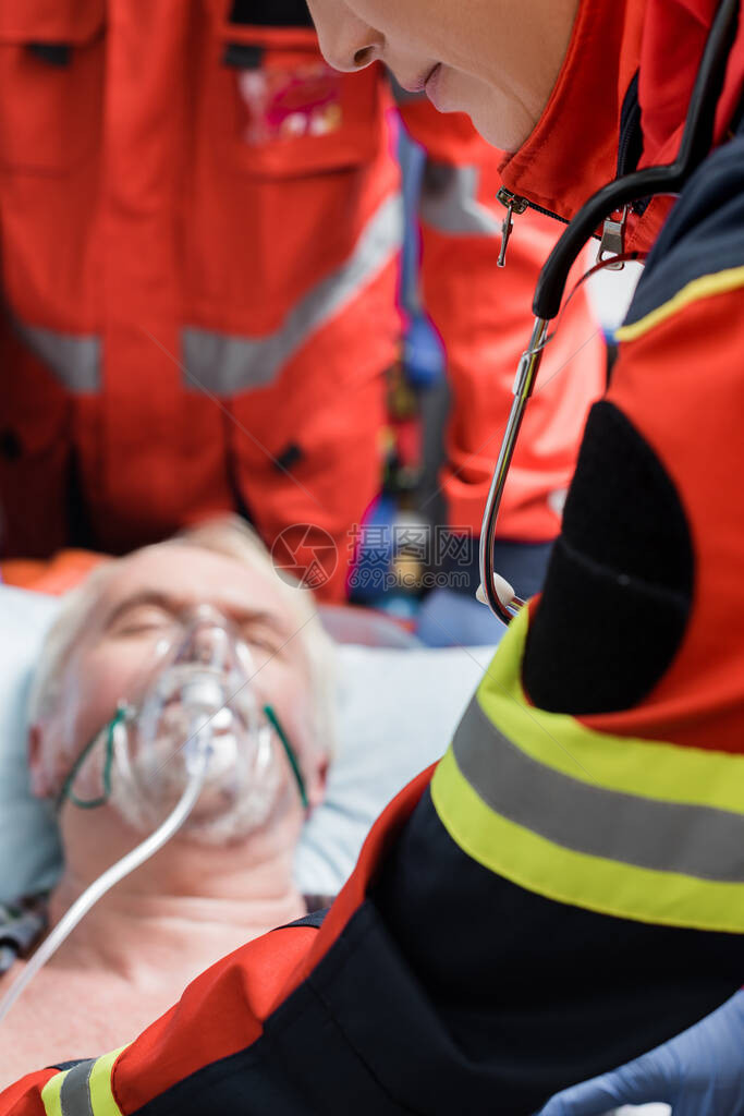 急救期间穿着制服站在戴氧气面罩的老人附近的护理人员图片