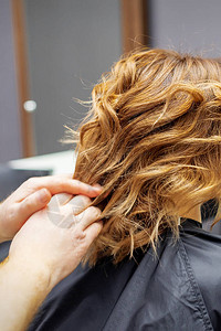 发型师为年轻女做发型红卷发和智能手机在图片